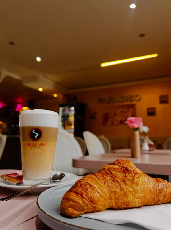 Latte Macchiato im Glas mit frischem Croissant vor dem PARADISO-Schriftzug